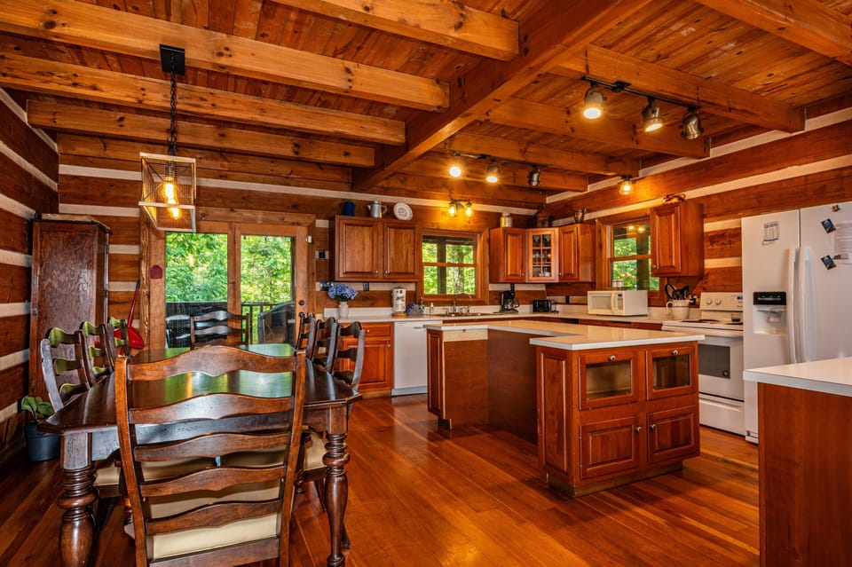 Dining area with dark wood table and chairs adjacent to kitchen featuring wood cabinets and white appliances.