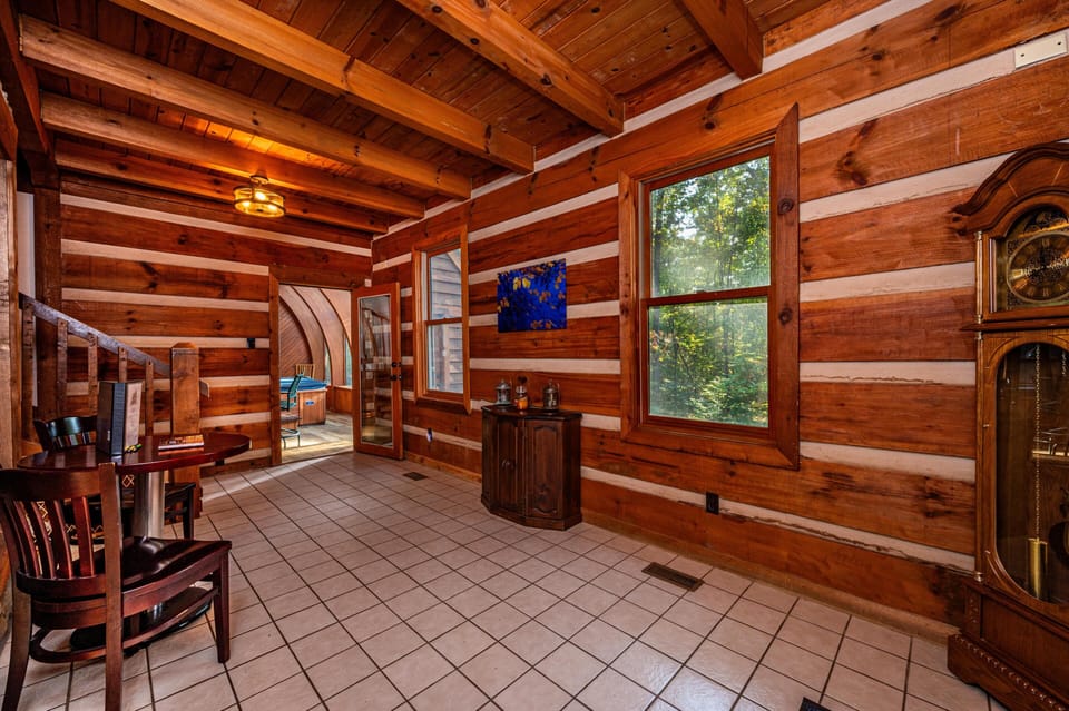 Entryway with white tiled floor, exposed log walls, wooden staircase, and view into a hot tub room.