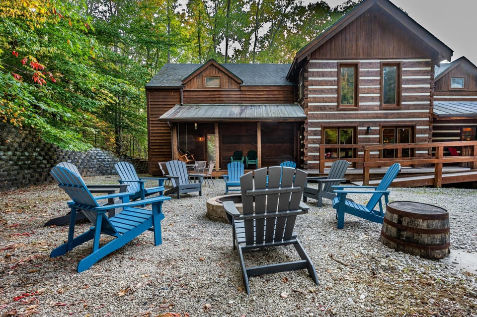 Outdoor seating area on gravel with blue and gray Adirondack chairs arranged around a stone fire pit near the log cabin.
