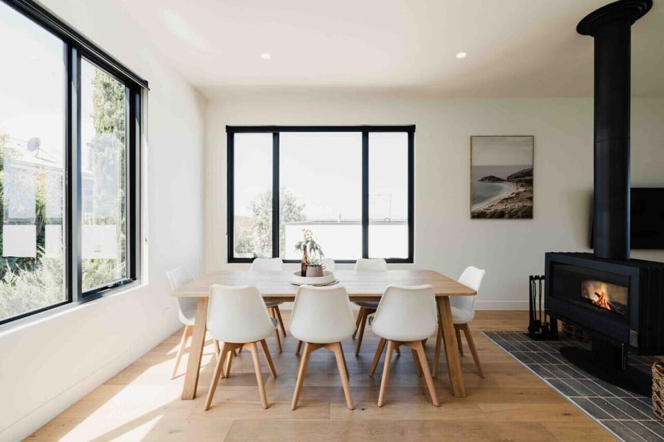 Light-filled dining area with sleek furnishings, expansive windows, and a warm fireplace