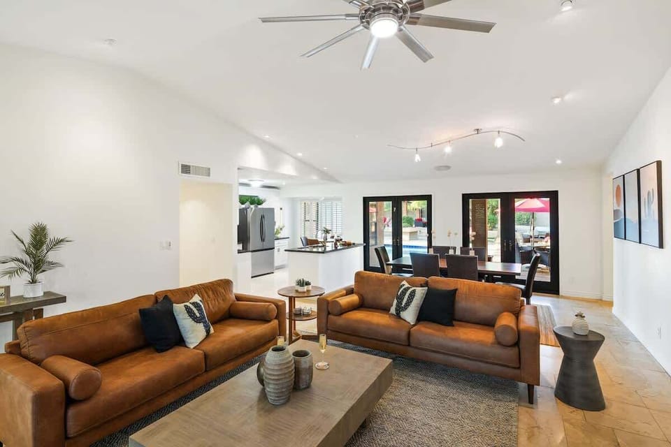 Bright open floor living space featuring a smart flat-screen TV, designer furnishings, and access to the outdoor patio leading to the attached casita and pool/spa area. Fireplace not functional.