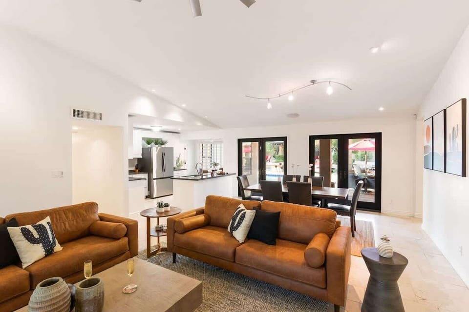 Bright open floor living space featuring a smart flat-screen TV, designer furnishings, and access to the outdoor patio leading to the attached casita and pool/spa area. Fireplace not functional.
