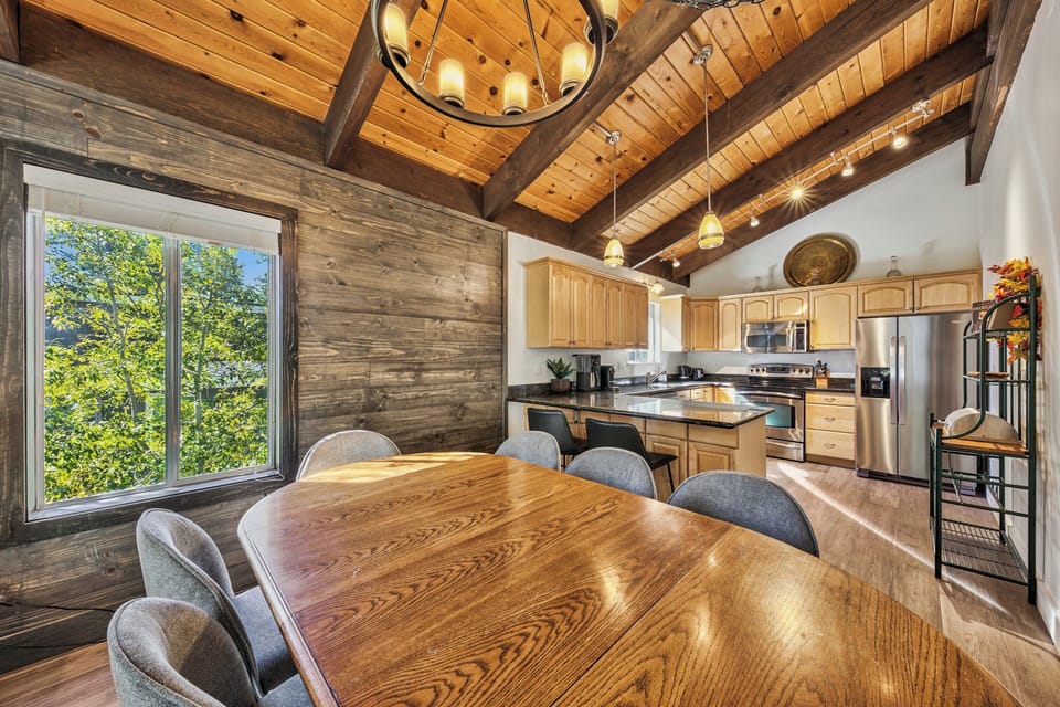 Gather around the stunning wood dining table beneath vaulted ceilings, where warm beams and rustic charm create the perfect setting for your memorable meals.