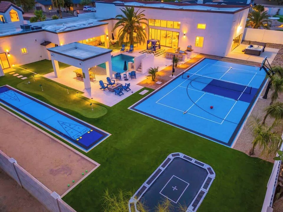 Modern luxury vacation property featuring extensive outdoor entertainment amenities including full-size sports court, swimming pool, covered patio, and multiple recreation areas set in a residential neighborhood.