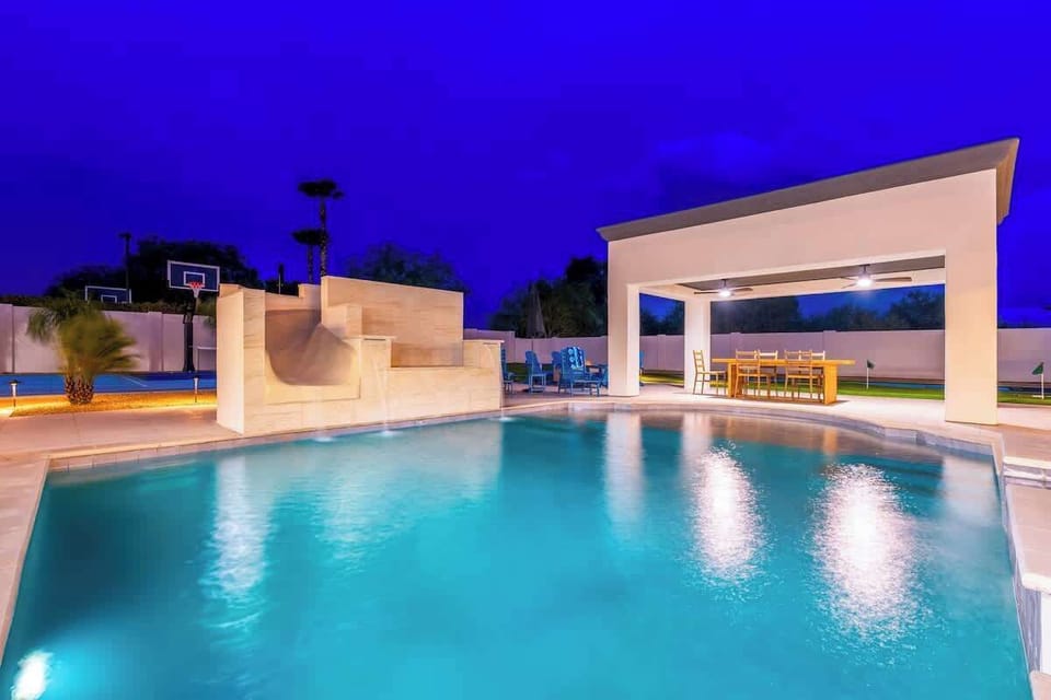 A stunning twilight view of the backyard features a pristine pool, covered dining pavilion, and sports court—ideal for evening gatherings and year-round fun.