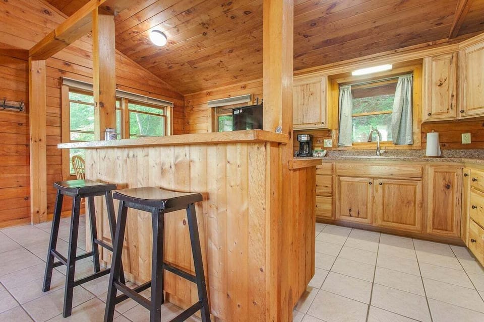 Open kitchen with natural wood cabinetry and a breakfast bar with seating. The layout connects the kitchen and living spaces for convenient gathering.