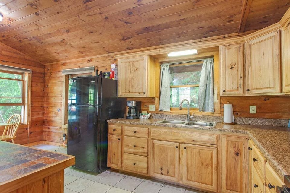 Full kitchen featuring granite countertops, wood cabinets, and modern appliances. Large windows bring natural light into the cabin's cooking space near Bryson City.