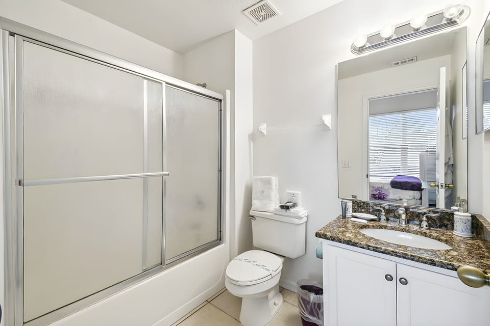 Bright and airy, this bathroom features sleek glass doors and a stylish granite countertop that adds a touch of sophistication. Enjoy the convenience of ample storage while basking in natural light through the large window.