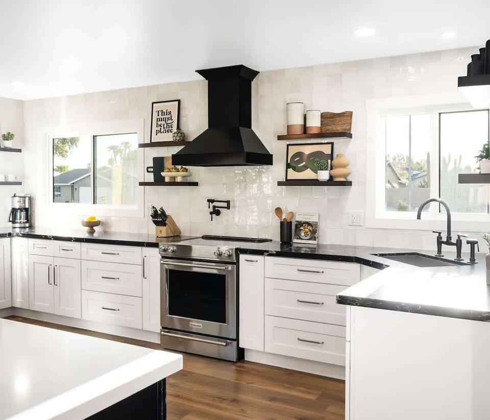 Modern kitchen fully equipped with stainless steel appliances, pot filler, crisp white cabinets, bold black marble countertops, and a spacious island.