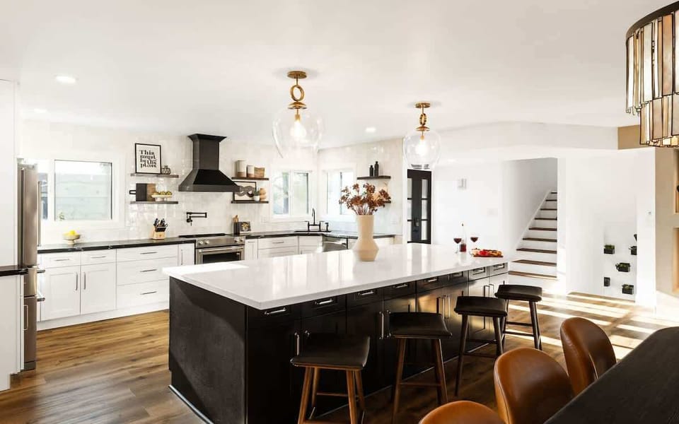 Modern kitchen fully equipped with stainless steel appliances, pot filler, crisp white cabinets, bold black marble countertops, and a spacious island.