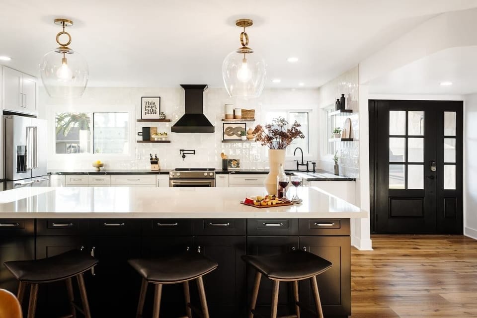 Modern kitchen fully equipped with stainless steel appliances, pot filler, crisp white cabinets, bold black marble countertops, and a spacious island.