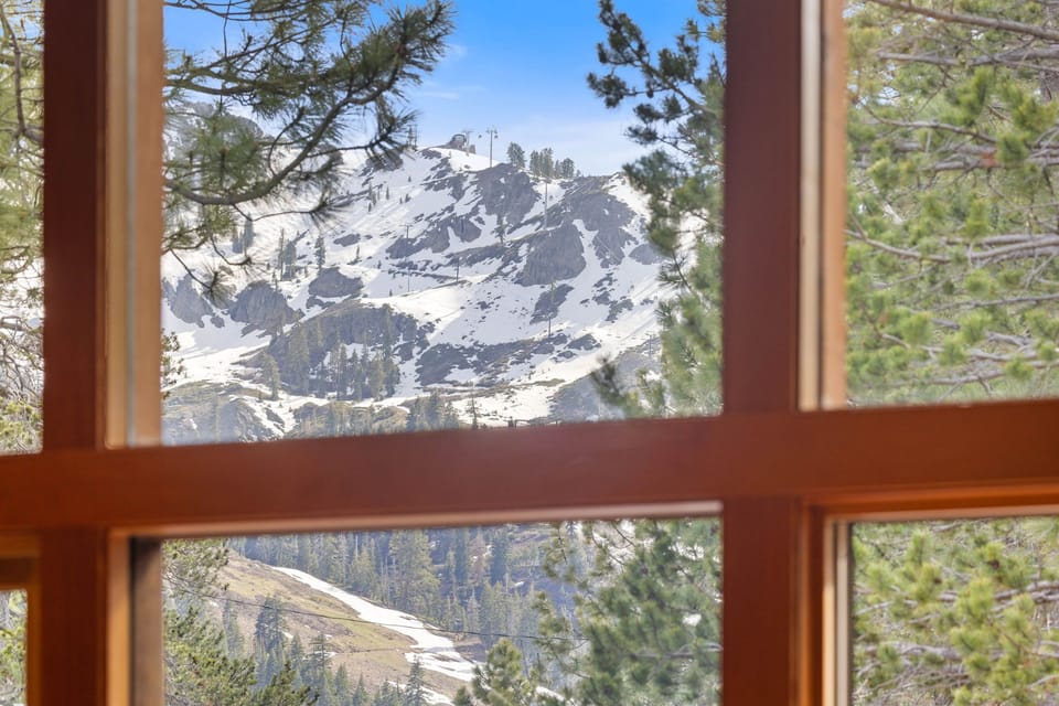 Panoramic mountain view framed by evergreens reveals snow-dusted peaks just beyond your window, blending alpine beauty with cozy warmth inside.