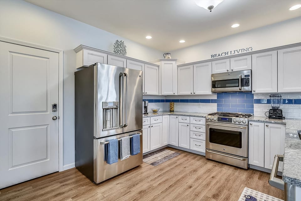 Your fully equipped kitchen features stainless steel appliances, coastal blue tile backsplash, and granite counters—perfect for preparing fresh meals during your beach getaway.