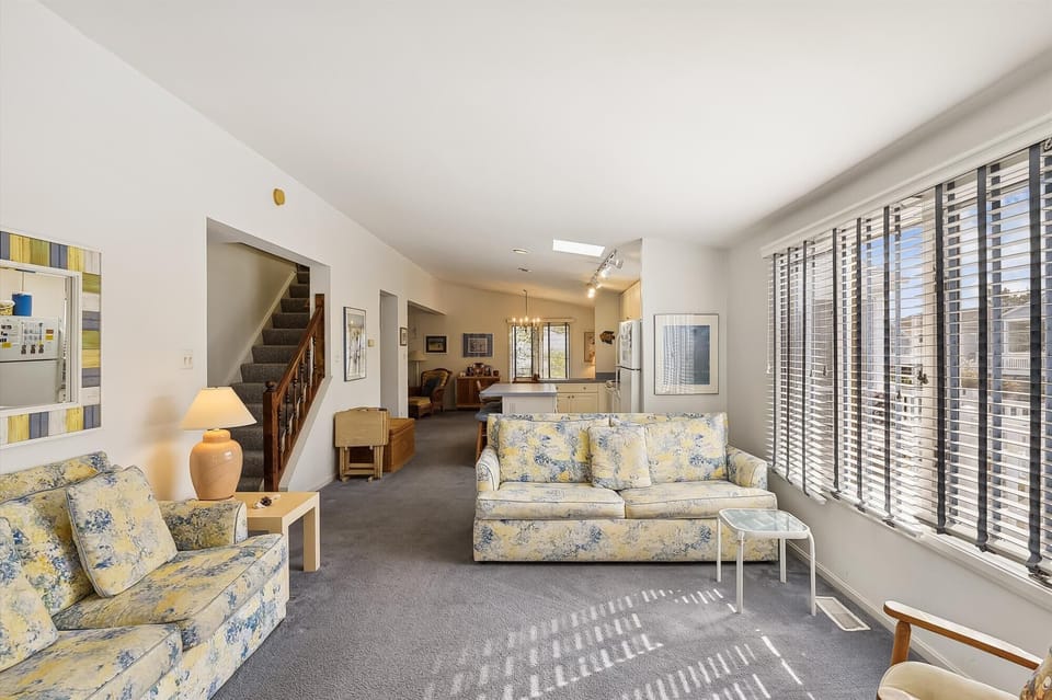 Settle into your spacious living room with comfortable floral sofas and bright natural light streaming through plantation shutters, creating a warm and welcoming retreat for relaxation.