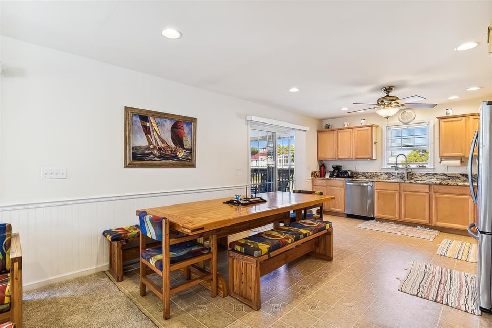 Gather around the warm wooden dining table in your sunlit kitchen, where vibrant cushions and coastal art invite you to share meals together, creating vacation memories that last a lifetime.