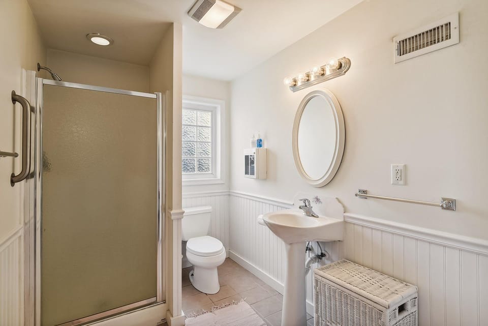 Step into your spotless private bathroom, where charming beadboard wainscoting and bright vanity lighting create a fresh, inviting space for your morning routine.