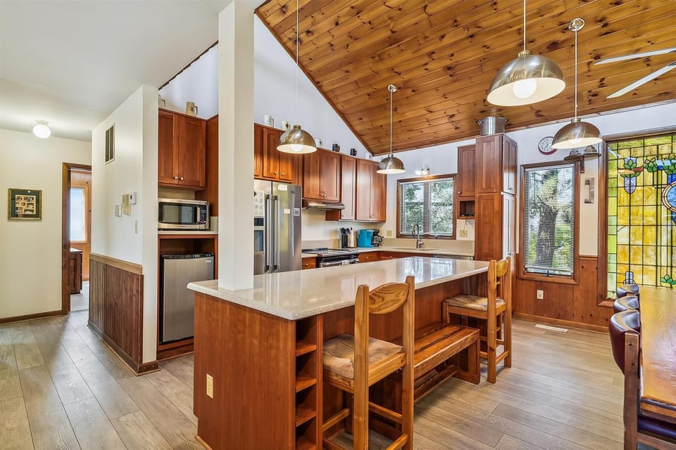 Gather with loved ones in this inviting kitchen featuring warm wood cabinetry, a spacious island with seating, and stunning knotty pine ceilings. Natural light streams through large windows, creating your perfect space to cook and connect.