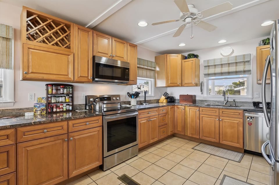 Your spacious, fully-equipped kitchen invites home-cooked meals with granite counters, stainless steel appliances, and a handy wine rack above. Picture morning coffee with sunlight streaming through plaid-lined windows.