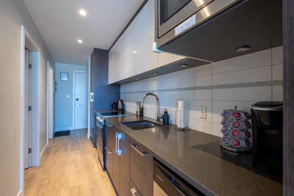 Modern kitchen galley equipped with full-sized stainless steel appliances, electric range, and solid countertops.