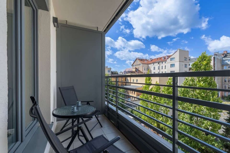 Outdoor balcony with a small table and chairs overlooking a green courtyard.