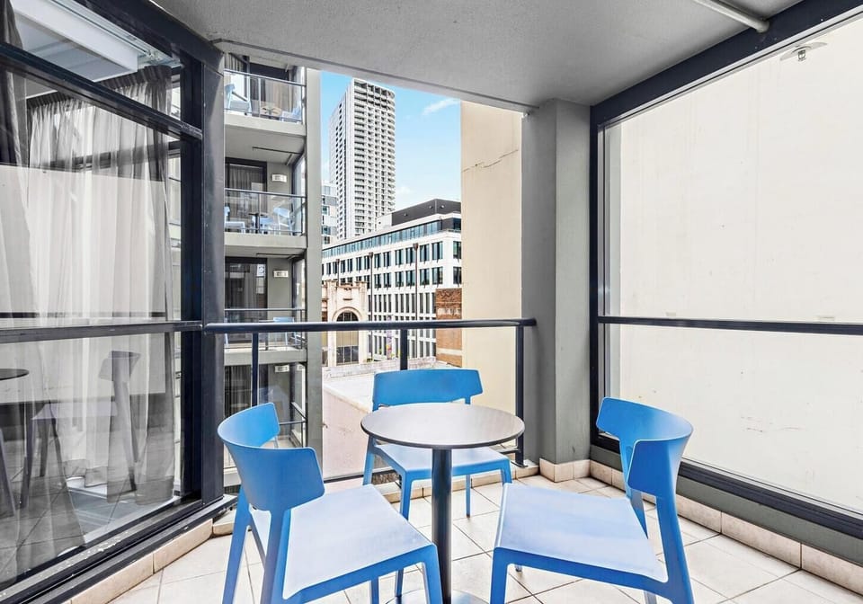 An outdoor tiled balcony equipped with white leisure chairs, looking out over a dense arrangement of city skyscrapers under a bright blue sky.