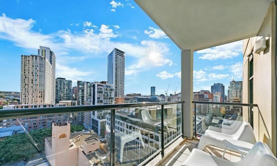 An outdoor balcony setup with white chairs, looking out over a densely populated city under a clear blue sky.