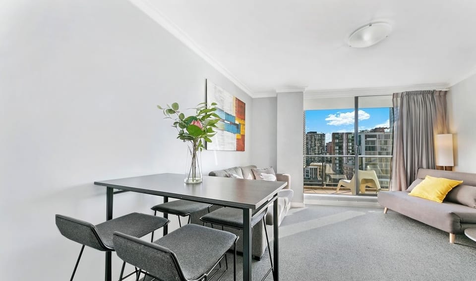 A stylish high-top dining table with four stools, positioned near a large window that frames the urban skyline.