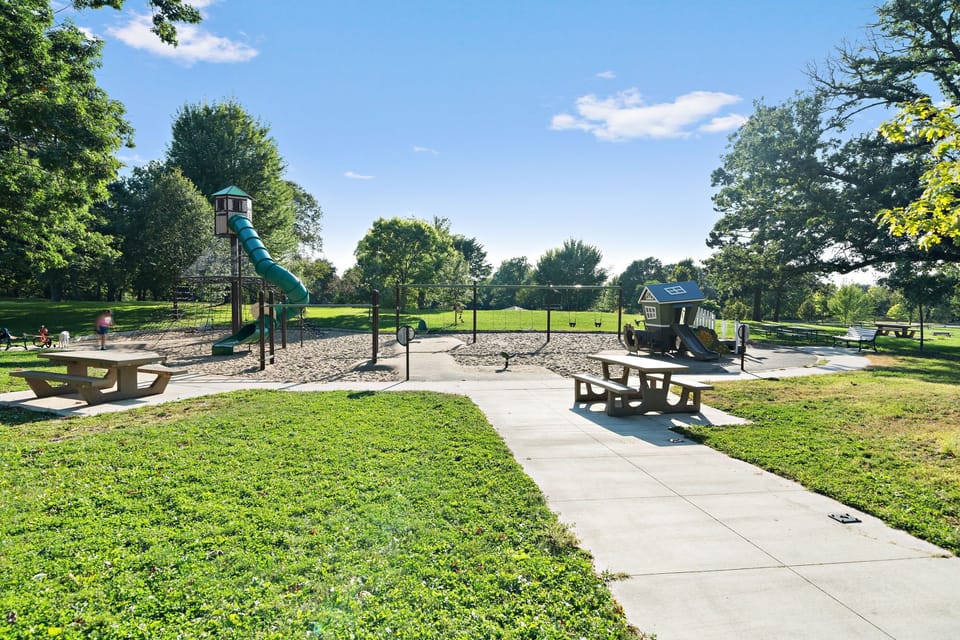 Community playground and picnic area surrounded by mature trees and open green spaces.