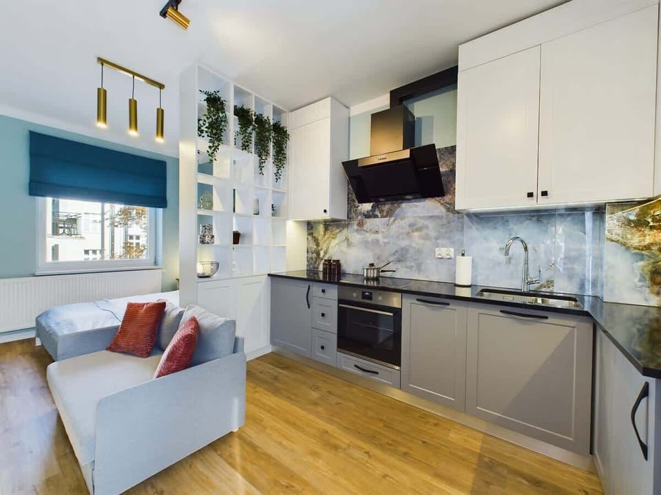 A spacious and modern living room with an elegant kitchenette, decorative plants, and a cozy sofa creates a stylish space for relaxing and cooking.