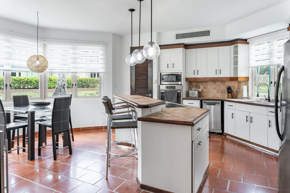 Fully equipped, Double-door refrigerator with ice-maker, Flush-top induction stove on center, tiled island serviced by two high-top bar stools.