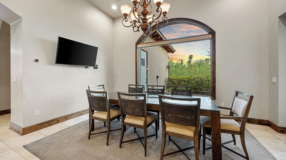 Elegant dining area with a glass-top table, arched window, and chandelier.