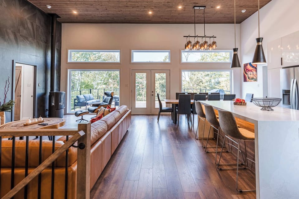 Open-concept kitchen, dining, and living area with floor-to-ceiling windows and forest views.