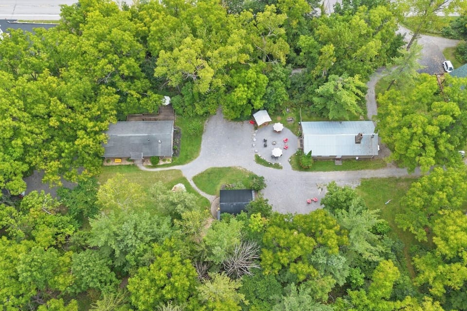 Kamp Kontent - A bird’s-eye view of the cozy cabins and communal outdoor fire pit, nestled within the wooded property. Perfect for large groups or families looking to enjoy the great outdoors.