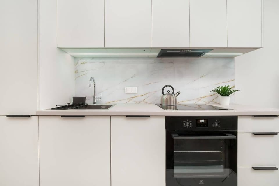 A minimalist kitchen with white cabinetry, integrated appliances, and a plant on the counter.

