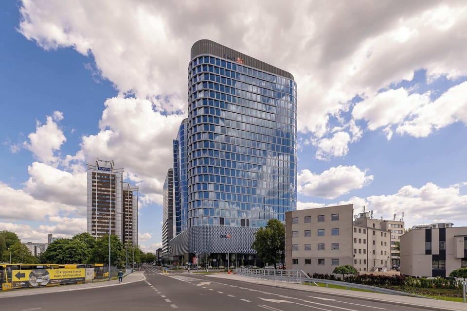 A futuristic office tower with a wavy glass façade rising over a landscaped plaza.

