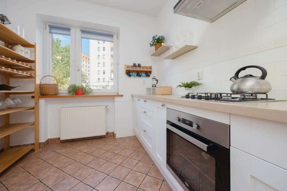 A kitchen with a large wooden dining table, simple white cabinets, and light terracotta tiles. The room feels spacious and practical.