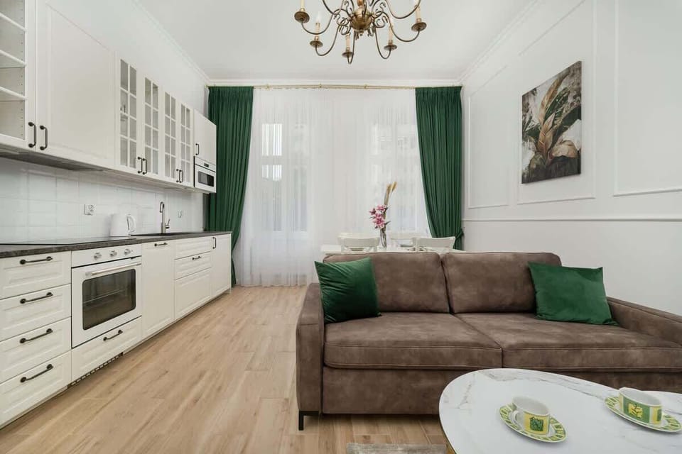 A spacious living room with a kitchenette, elegant curtains, and a comfortable sofa creates a harmonious and functional space for relaxing and preparing meals.