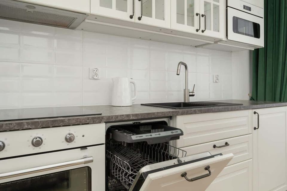 A white kitchenette with modern appliances and green curtains combines function and style.