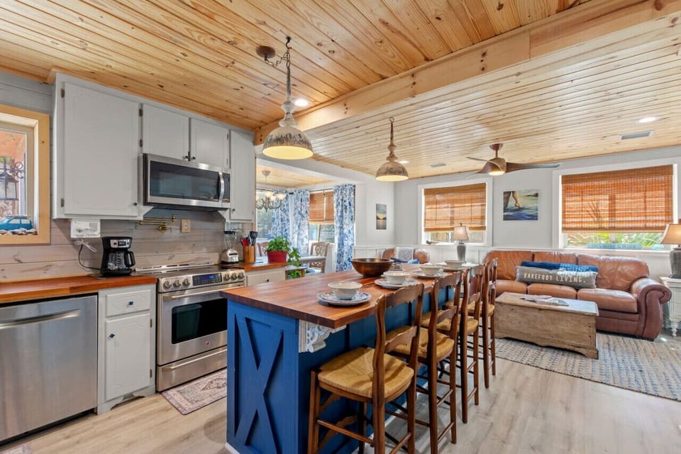 A beautifully crafted wood-designed kitchen with a blue island, spacious and open, featuring a lovely view of the living room and plenty of natural light.