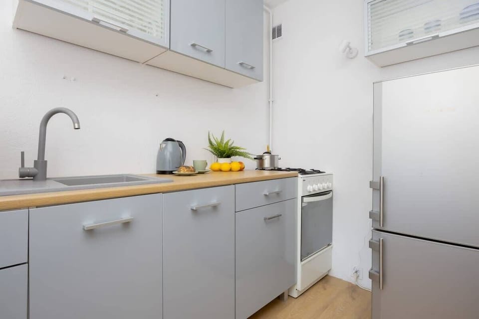 A minimalist kitchen with grey countertops, wooden shelves, and basic appliances.

