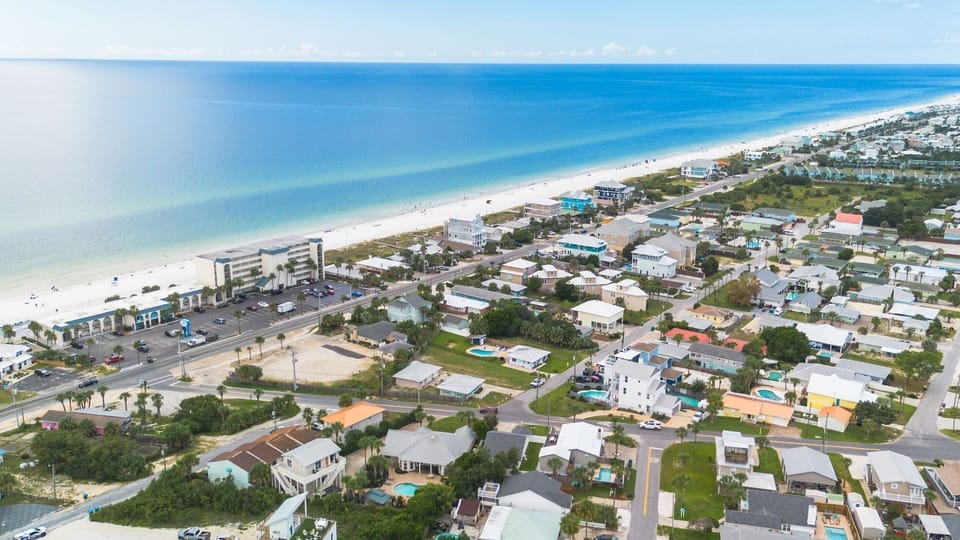 Stunning aerial view of a charming beachfront community with pristine white sand beaches and turquoise waters stretching to the horizon.