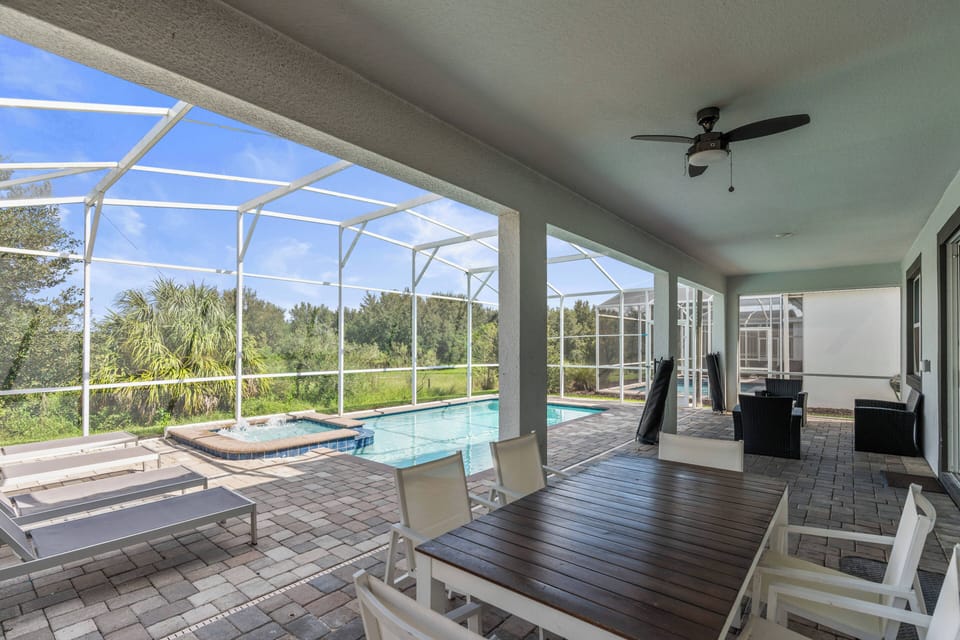 Enjoy the sunlit patio with a spacious dining table and cozy lounge chairs, ideal for relaxing afternoons by the pool. The screened enclosure adds to your outdoor experience with peaceful views of lush greenery.