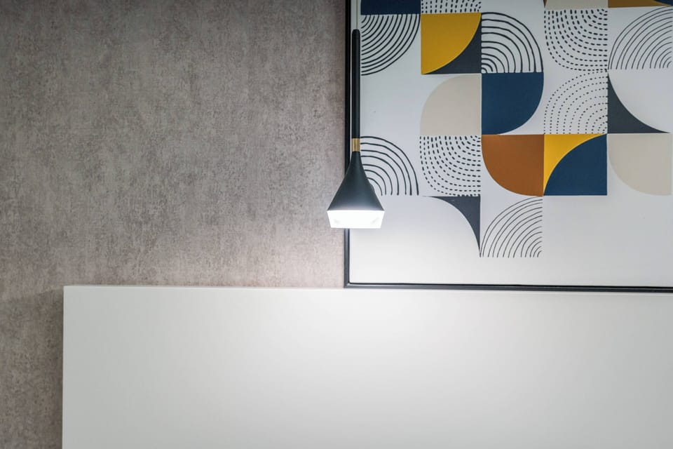 Brighten your stay in this stylish room, where a sleek pendant light casts a warm glow over a minimalist white surface. The contemporary artwork adds a pop of color with geometric patterns that complement the textured gray wall.