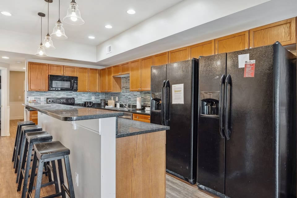 A modern kitchen with two side-by-side fridges, a spacious countertop with bar stools, and an abundance of cabinets—providing plenty of storage and a functional, stylish space for cooking and entertaining.
