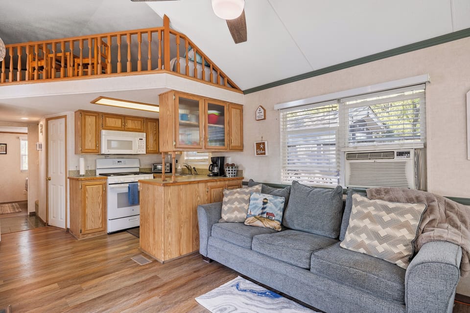 Standing back, this view showcases the airy, open-concept layout with the living area, cozy couch, loft above, and kitchen all in one inviting space.