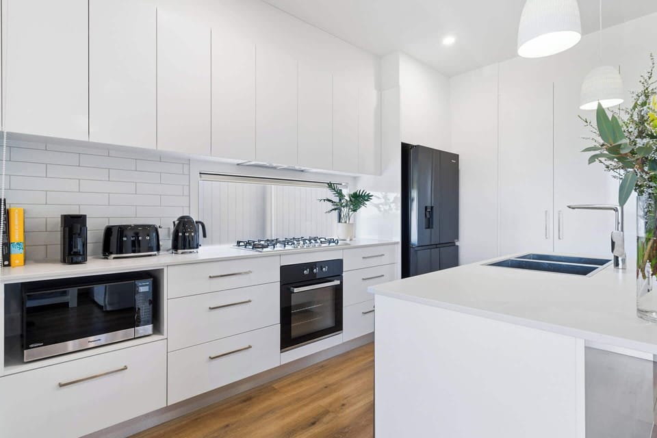 Step into this bright kitchen, featuring sleek white paint and modern appliances—oven, dishwasher, and fridge—perfect for effortless cooking and entertaining