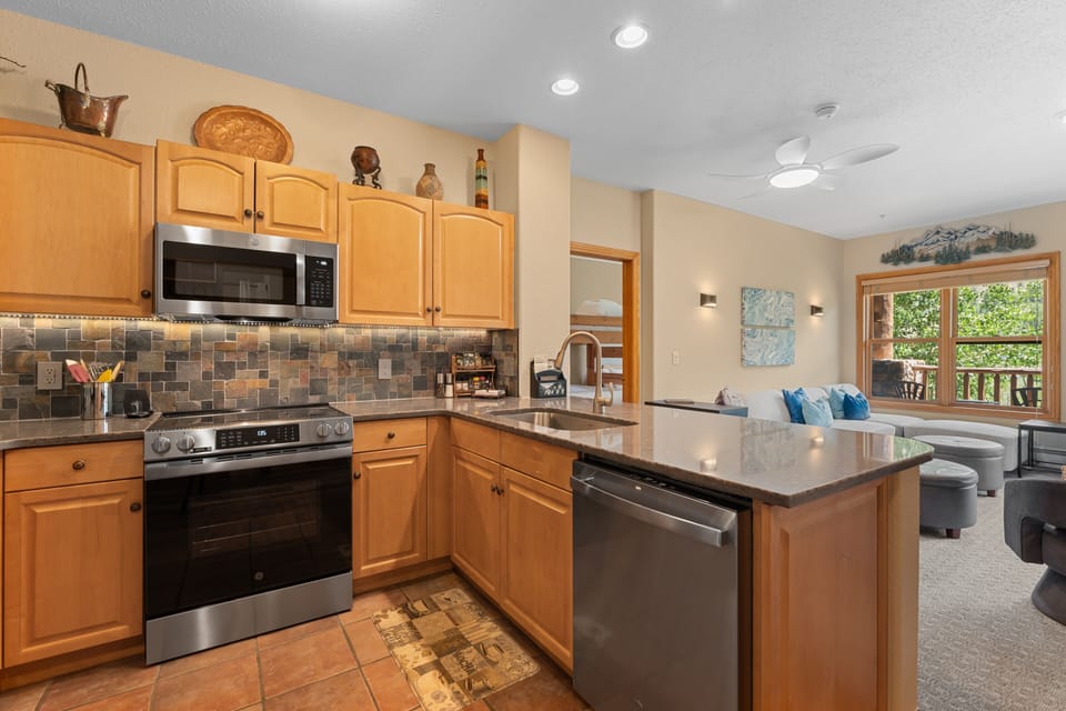 Your fully equipped kitchen features modern stainless appliances, warm wood cabinetry, and a spacious island perfect for gathering over meals while natural light streams through the windows.