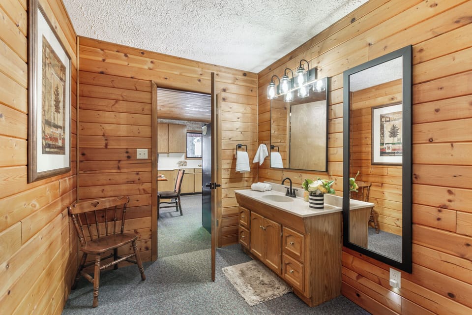 Freshen up in style in this warmly designed bathroom, featuring natural wood walls, cozy lighting, and thoughtful touches at Raven's Retreat.
