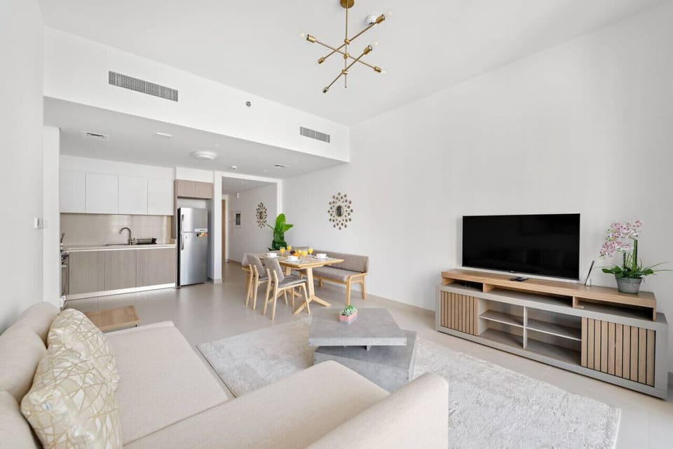 Open-plan apartment living room with a sofa, TV, dining area, and kitchen.