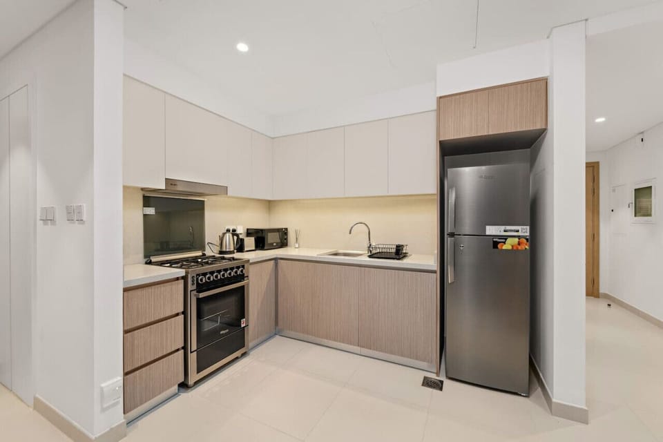 Modern kitchen with light wood cabinets, stainless steel appliances, and tiled floor.